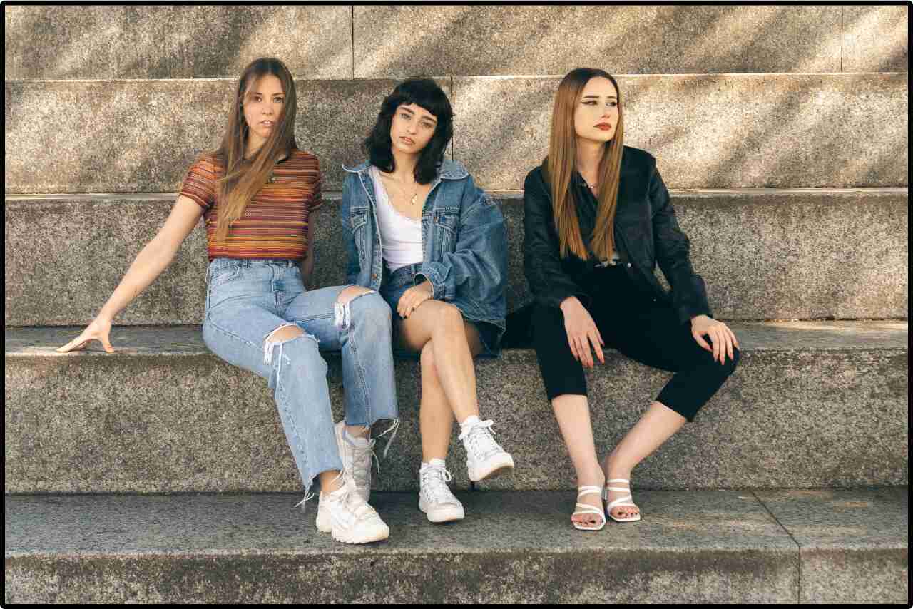 Group of friends in casual summer clothes, smiling and sitting on the stairs.